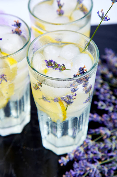 Lavender lemonade with lemon and ice on black background. Detox water. Summer drink. Diet cocktail. Beautiful. - Фото, изображение