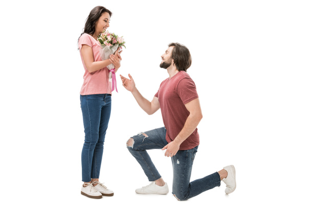 Zijaanzicht van vrouw met boeket van bloemen en man die op één knie geïsoleerd op wit - Foto, afbeelding