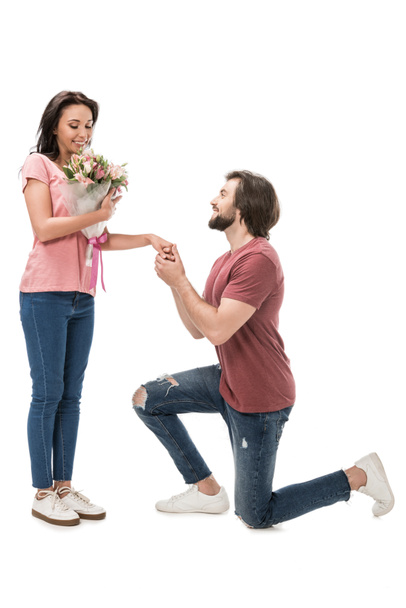 вид сбоку женщины с букетом цветов и мужчины, стоящего на одном колене, изолированного на белом
 - Фото, изображение