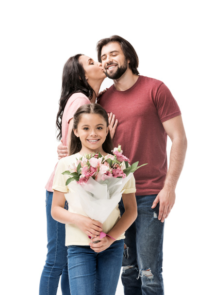 portrait of smiling daughter with bouquet of flowers with parents kissing behind isolated on white - Photo, Image
