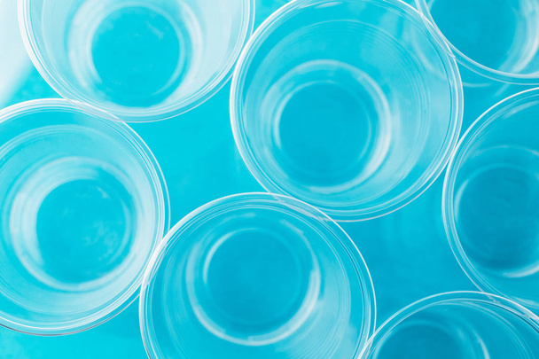 Vista superior de los nuevos vasos de plástico desechables transparentes vacíos limpios sobre fondo azul brillante
 - Foto, Imagen