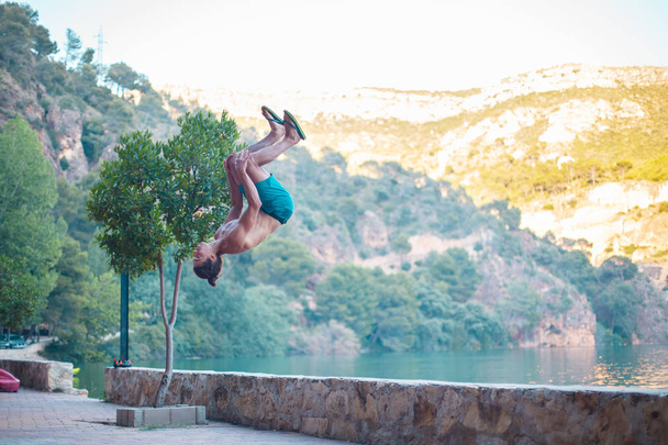 Mladý muž dělá Boční přetočení nebo Salto když trénují parkour na jezeře v přírodě.  - Fotografie, Obrázek