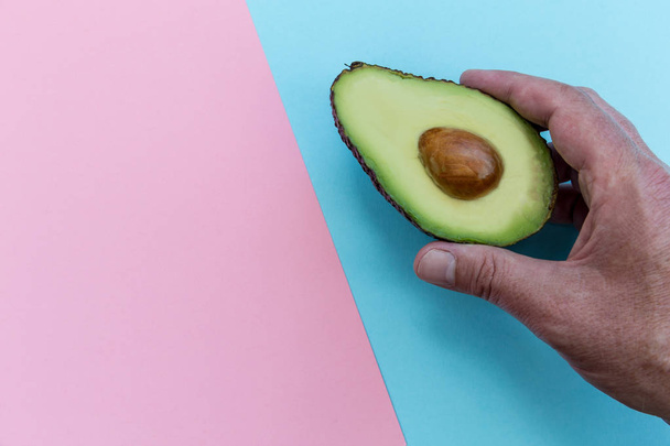 Hand holding avocado half on bright pink and blue background  - Photo, Image