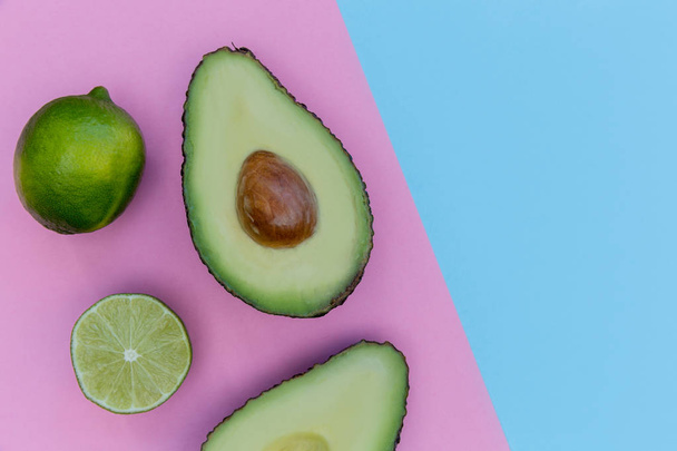 Avocado halves and limes on bright pink and blue background background  - Foto, Imagen
