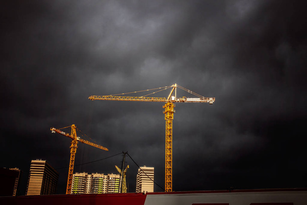 Крани на будівельному майданчику проти драматичного неба
 - Фото, зображення