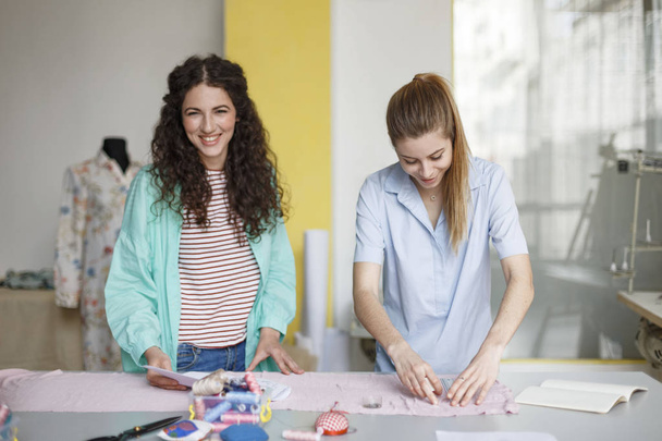 Kauniit nuoret suunnittelijat työskentelevät onnellisesti yhdessä uuden tekstiilin kanssa modernissa ompelutyöpajassa
 - Valokuva, kuva