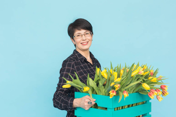 Floristin mittleren Alters hält blaue Holzkiste mit Tulpen im Atelier - Foto, Bild