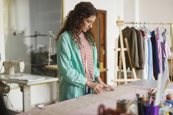 Молодий продуманий дизайнер готує роботу з новим текстилем у затишній швейній майстерні
 - Фото, зображення