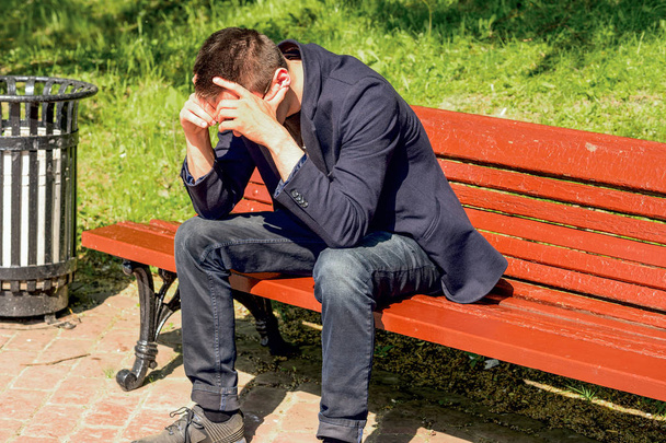 young man sitting on bench in park, covering his face with his hands - Foto, immagini