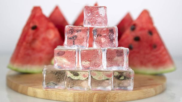 Berry watermelon in water splashes. Cubes of ice in droplets of water are stacked in a pyramid. White background on photo. - Foto, Bild