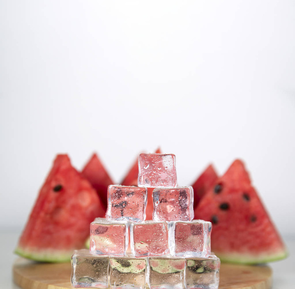 Berry watermelon in water splashes. Cubes of ice in droplets of water are stacked in a pyramid. White background on photo. - Photo, image