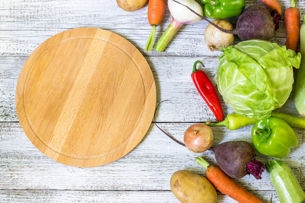 top view of circle cutting board, knife and fresh vegetables on wooden table top. - Photo, image