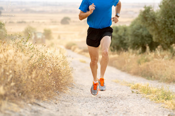 close up man runner legs and feet of extreme cross country man running and training on rural track jogging at sunset with harsh sunlight and lens flare in countryside sport and healthy lifestyle. - Photo, Image