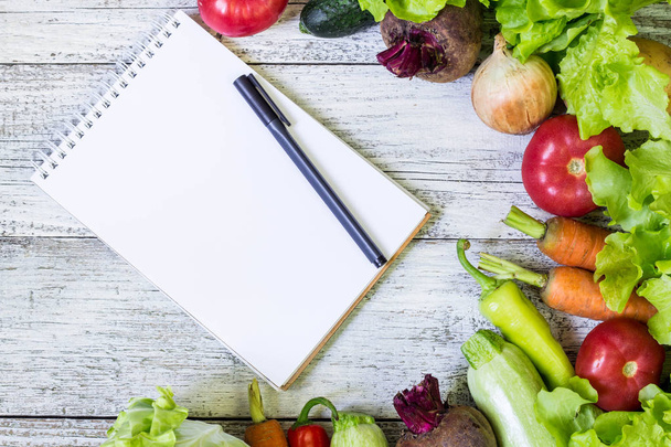 ジューシーな野菜の境界線、コピー スペースとペンを白い木製の背景、上面に白いメモ帳空白。健康料理レシピのモックアップ. - 写真・画像