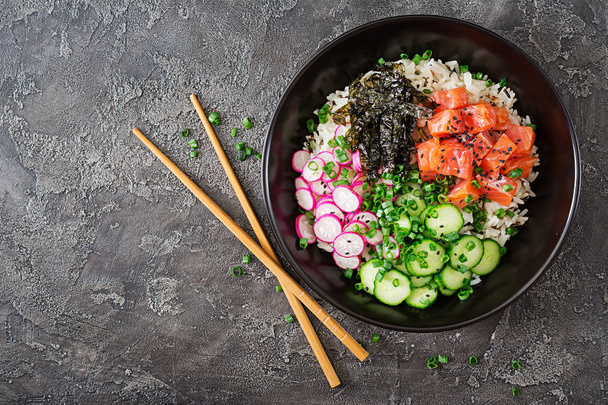 米、大根、キュウリ、トマト、ゴマ、海藻とハワイアンのサーモン ピンクの魚突くボウル。鉢の石仏。ダイエット食品。平面図です。フラットを置く - 写真・画像
