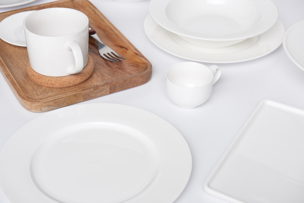 close up view of wooden tray, fork with various plates and cup with bowl on white table - Foto, Bild