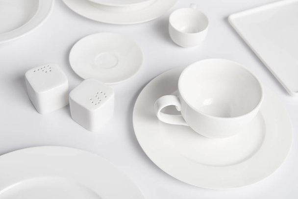 close up image of different plates, cup, bowl, saltcellar and pepper caster on white table  - Foto, Imagen