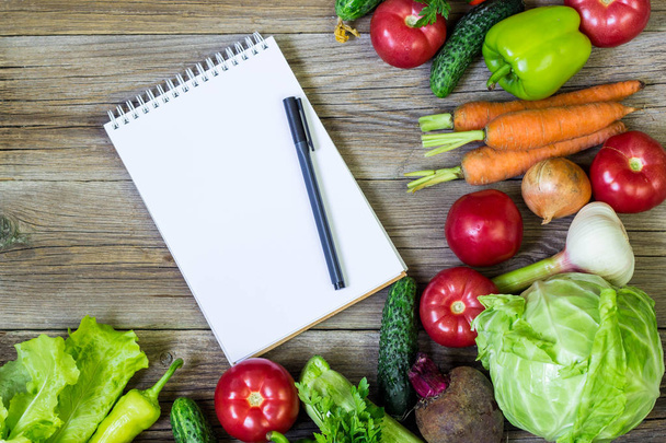 ジューシーな野菜の境界線、コピー スペースと木製の背景、平面図上にペンと白いメモ帳空白。健康料理レシピのモックアップ. - 写真・画像