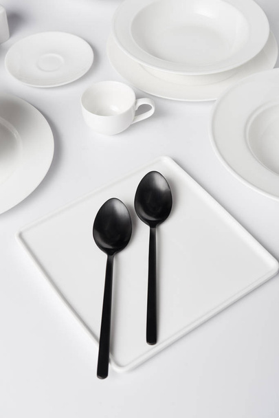selective focus of various plates, two spoons and cup on white table - Foto, afbeelding