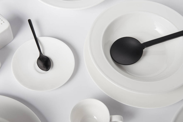 close up image of various plates, spoon, cup and salad spoon on white table - Фото, изображение