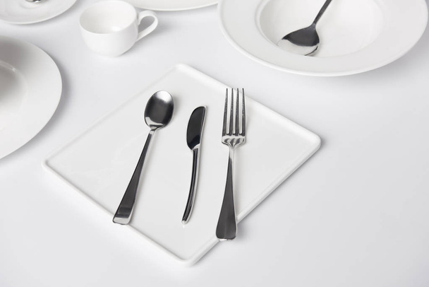 enfoque selectivo de varios platos, taza, tenedor, cuchillo y cucharas en la mesa blanca
 - Foto, Imagen