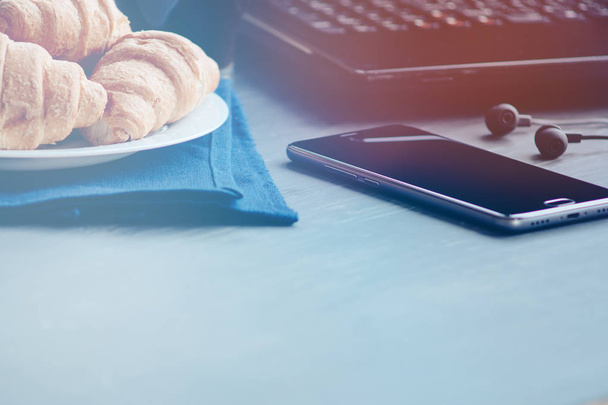 Close-up van houten desktop met koffie, croissant, telefoon met, licht toning - Foto, afbeelding
