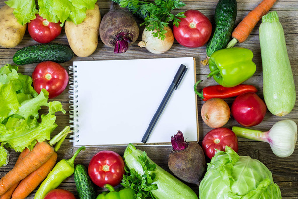 frisches saftiges Gemüse Rand, leerer weißer Notizblock mit Kopierraum und Stift auf Holzgrund, Draufsicht. Attrappe für gesundes Gericht. - Foto, Bild