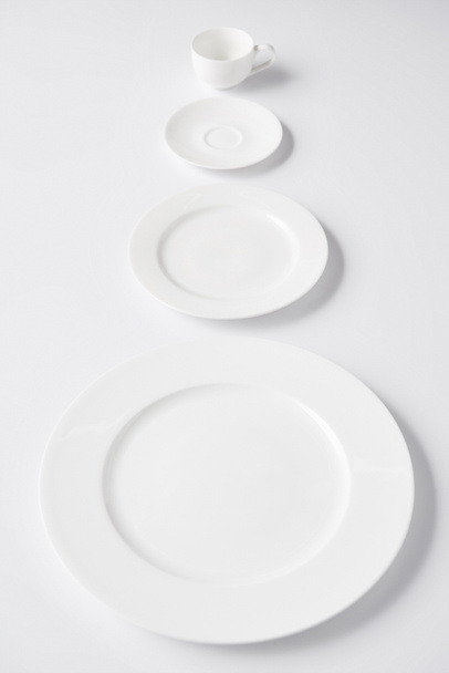 selective focus of arranged various plates and cup on white table - Foto, afbeelding
