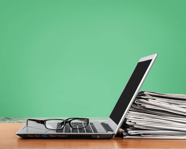 Laptop and black glasses ans stack of newspapers  - Фото, изображение