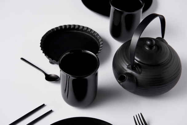 selective focus of black teapot, cups, fork, spoon, chopsticks and baking dish on white table - Photo, Image