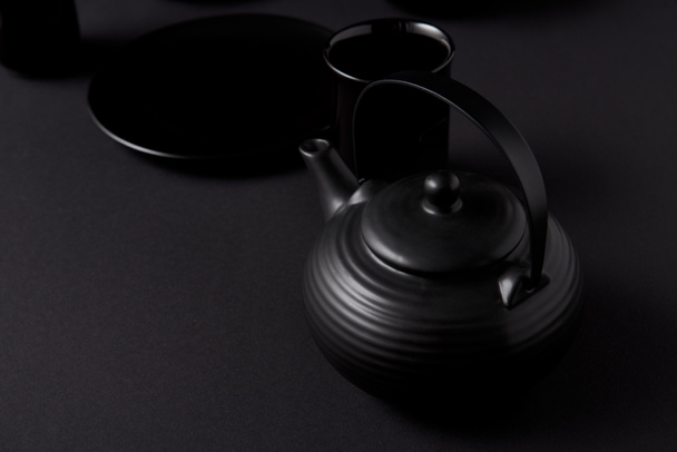 selective focus of black teapot, cups and plate on black table  - Фото, изображение