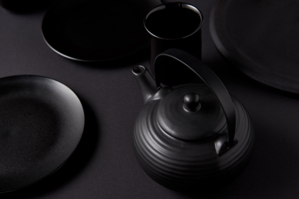 selective focus of black teapot, cup and plates on black table  - Fotó, kép