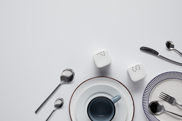 top view of saltcellar, pepper caster, spoons, knife, fork, cup and plates on white table - Fotó, kép