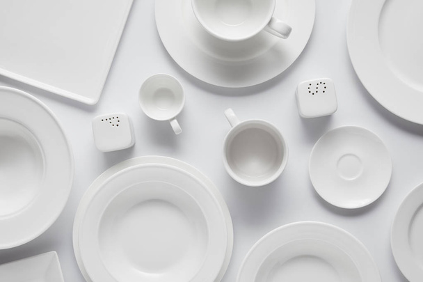 top view of various plates, bowl, saltcellar, pepper caster and cups on white table - Foto, Bild