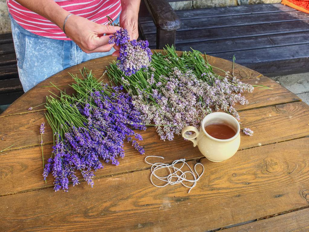 Las manos de la mujer jardinero crear aroma relajante ramo de hierbas. Mesa de trabajo con té de hierbas, tallos de lavanda y tijeras
. - Foto, Imagen