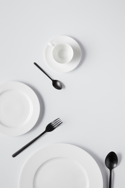 top view of plates, cup, fork and black spoons on white table  - Foto, Bild