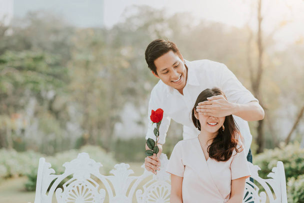 Aziatische man verrast zijn vriendin met bloem van achteren - Foto, afbeelding