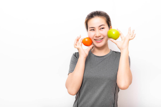 Asian woman with detal braces having fun with green apple and tomato on white background - Φωτογραφία, εικόνα