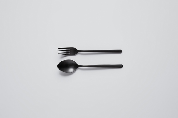 vista superior de cuchara negra y tenedor sobre mesa blanca, concepto minimalista
 - Foto, Imagen