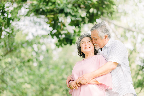 Happy Asian senior couple having a good time. They smiling while holding each other outdoor in the park. - Photo, Image