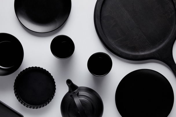 top view of black teapot, plates, bowl, baking dish and cups near tray on white table - Foto, afbeelding
