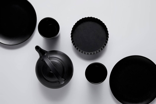 top view of black teapot, plates, baking dish and cups on white table - Photo, Image