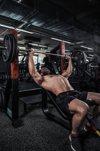 Portrait of a handsome muscular man doing bench press in fitness gym - Foto, imagen