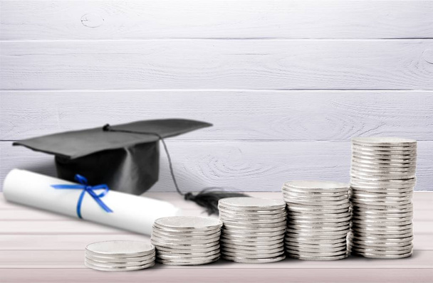Graduation hat and stacked coins on wooden table  - Foto, Bild