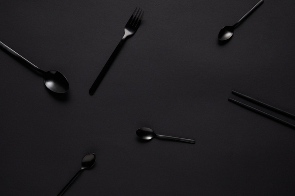 vista superior de varias cucharas negras, tenedor y palillos en la mesa negra
  - Foto, Imagen