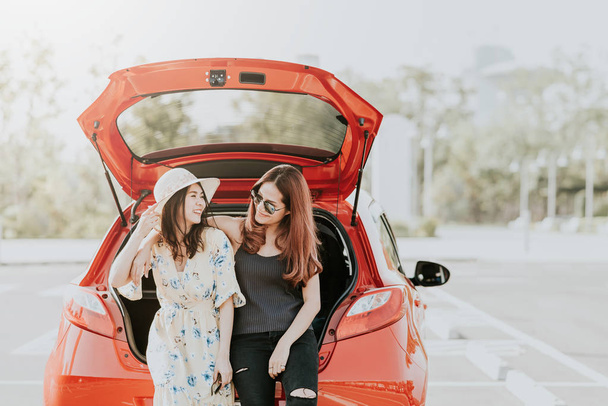 Menina asiática feliz melhores amigos viajante rir e sorrir juntos enquanto sentado no porta-malas do carro durante as férias
 - Foto, Imagem