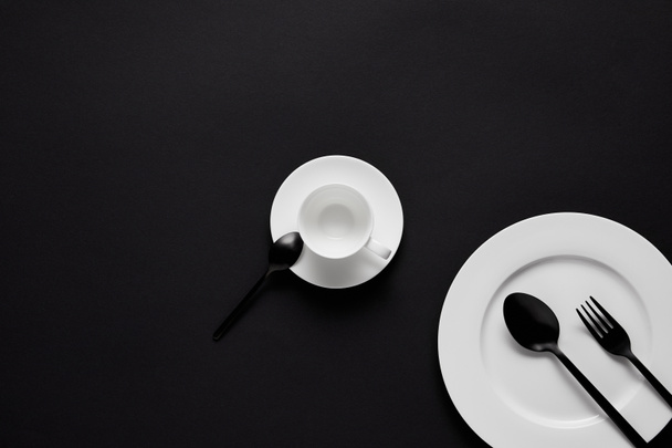 top view of plate, cup, black spoons and fork on black table - Foto, Bild