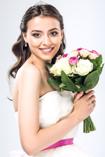 close-up portrait of beautiful young bride in wedding dress with earrings and tiara holding bouquet isolated on white - Fotografie, Obrázek