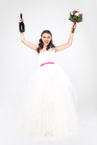 celebrando novia joven en vestido de novia con botella de champán y ramo de novia aislado en blanco
 - Foto, Imagen