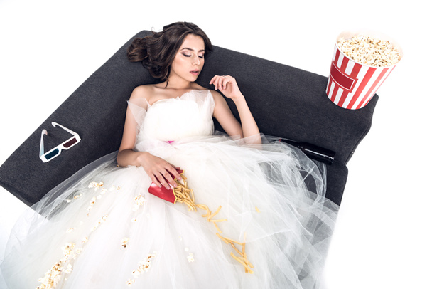 vista de ángulo alto de la novia joven en vestido de novia durmiendo en el sofá con comida chatarra aislada en blanco
 - Foto, Imagen